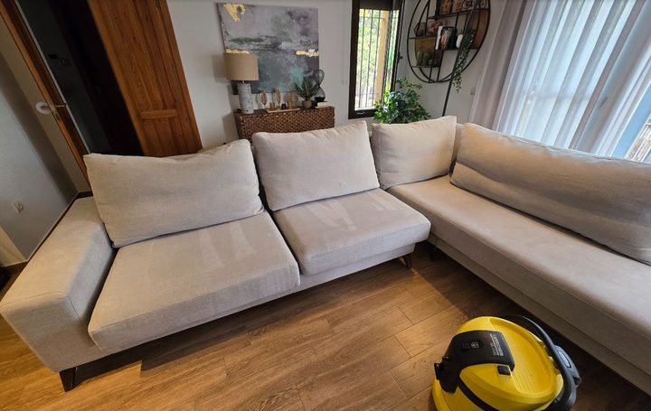 Sofá beige de salón recién limpiado, con la máquina todavía en el suelo