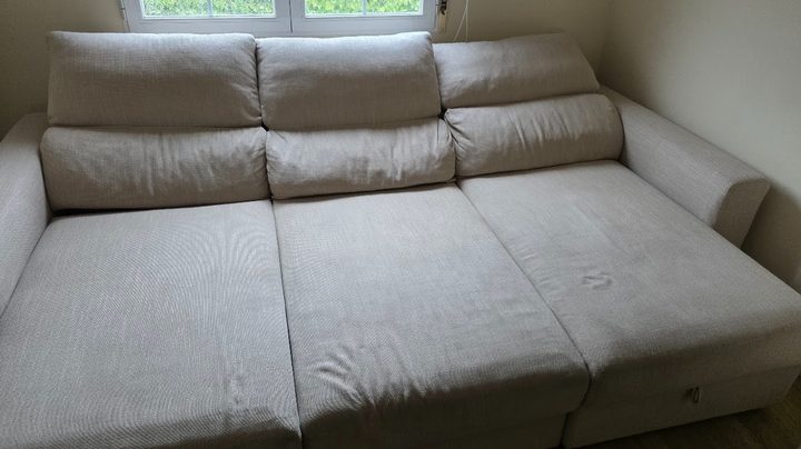 Sofá cama beige con marcas de uso, antes de la limpieza